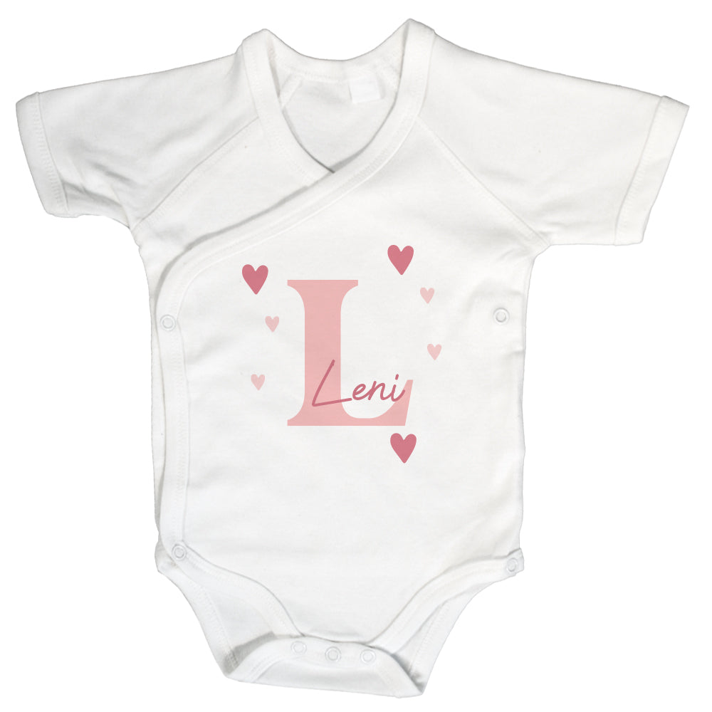 Weißer Wickelbody mit kurzem Arm, rosa Initiale „L“, Name „Leni“ und Herzmotiven auf weißem Hintergrund.