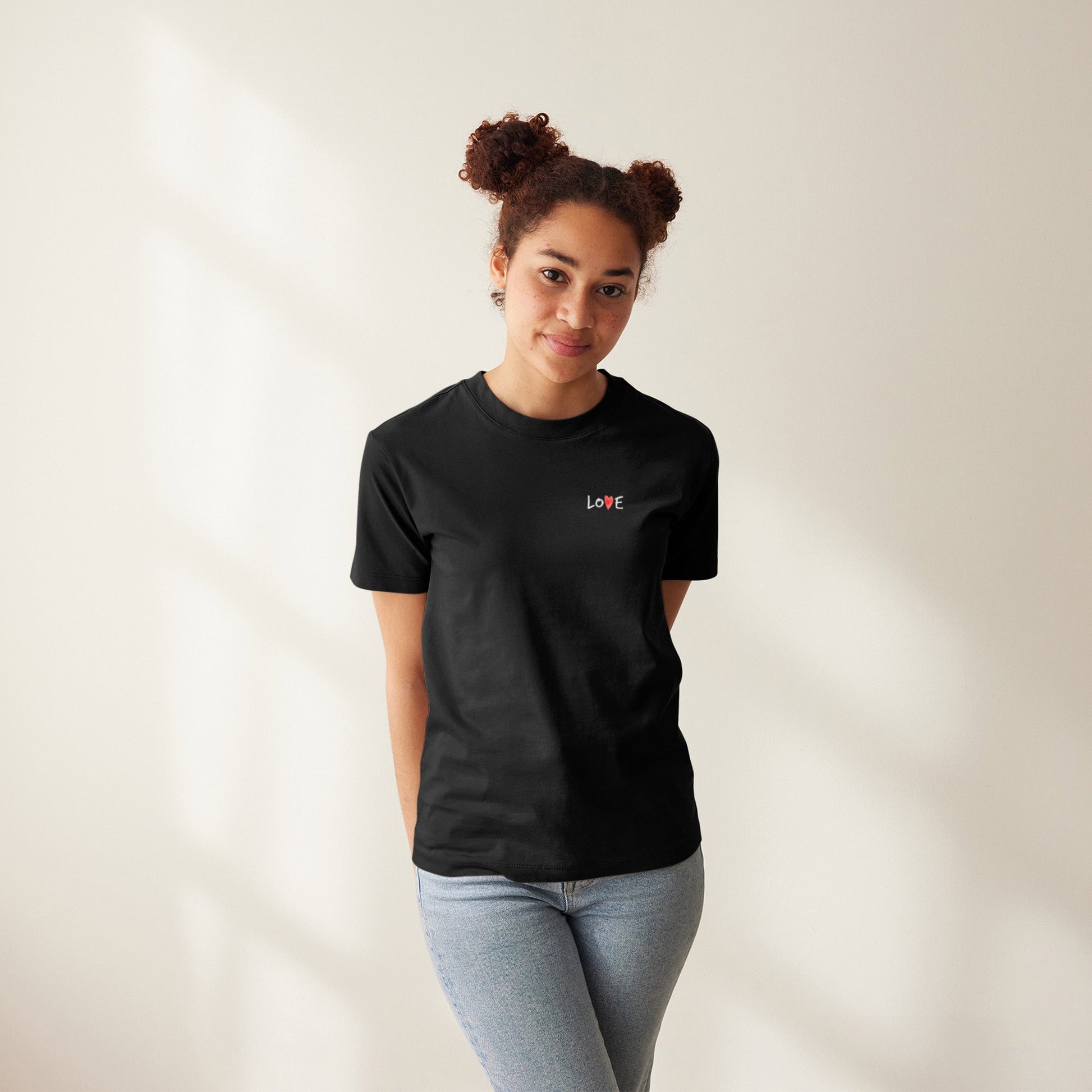Modell trägt schwarzes T-Shirt mit kleinem „LOVE“-Schriftzug auf Brusthöhe, das „O“ ersetzt durch ein rotes Herz. Auf der Rückseite großer Print „LOVE IS LOVE“ mit Regenbogenherzen - als Symbol für Stolz, Akzeptanz und die LGBTQIA+ Community.