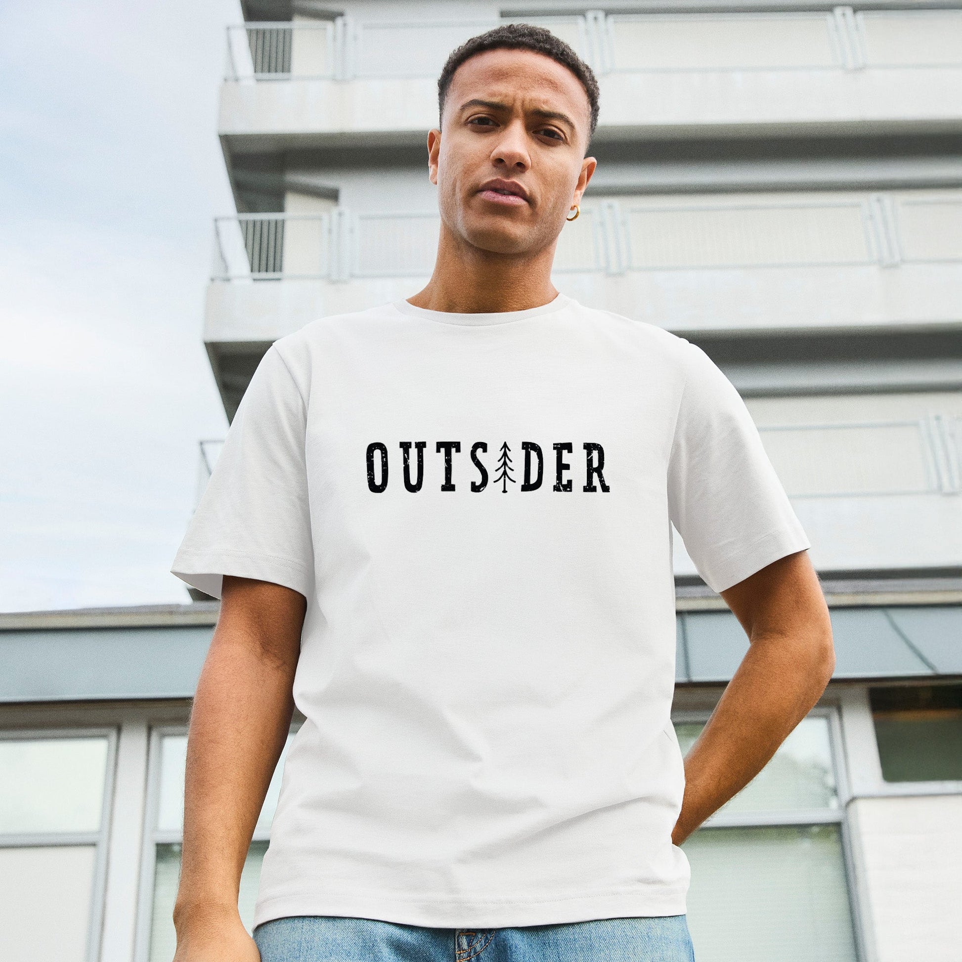 Modell trägt weißes T-Shirt mit Frontdruck „OUTSIDER“, bei dem das „i“ durch eine stilisierte Tanne ersetzt ist