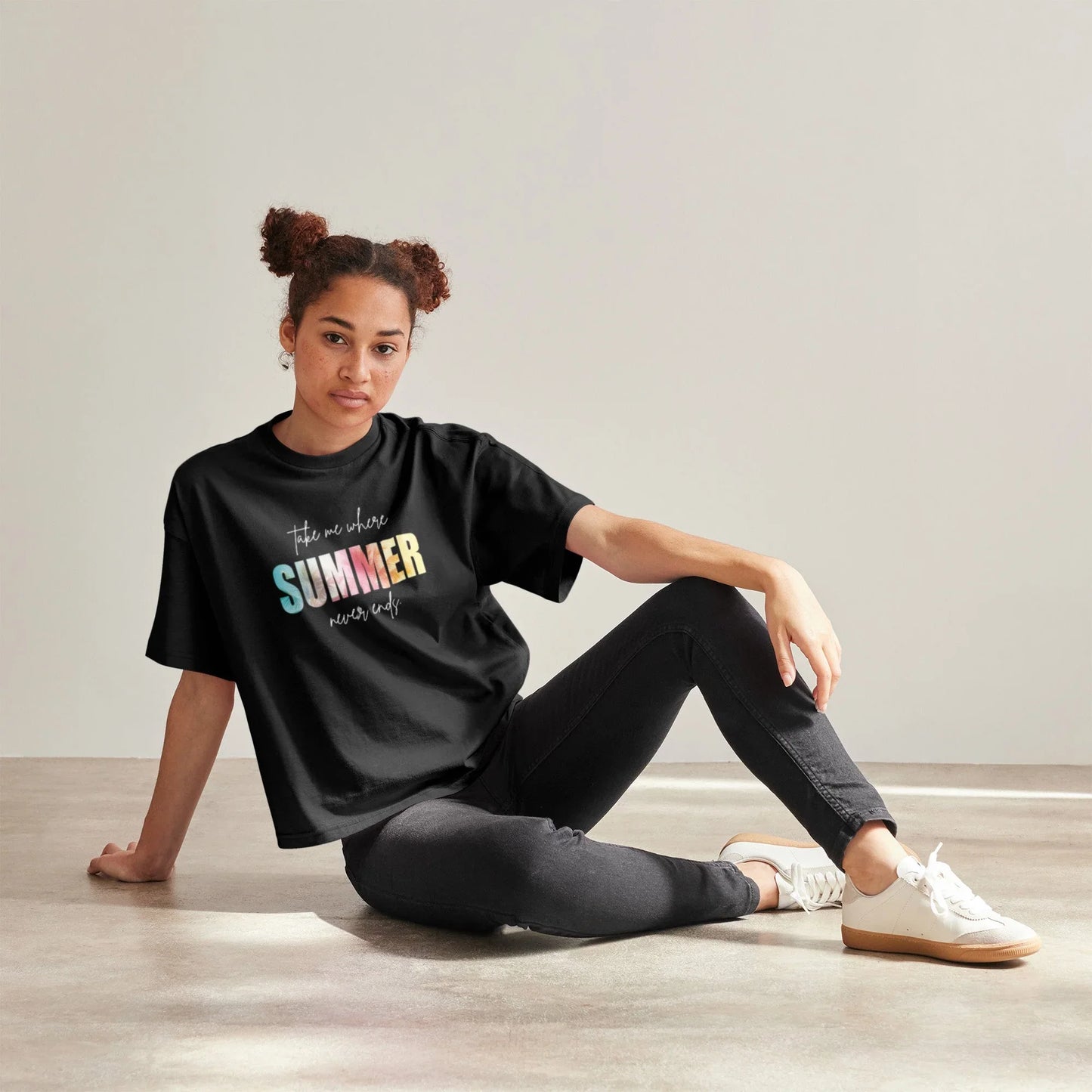 Frau sitzt entspannt im schwarzen T-Shirt mit bunter Aufschrift 'Summer never ends', schwarze Jeans