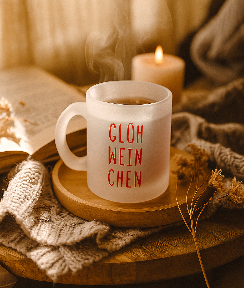 Handbedruckte Glastasse „Glühweinchen“ mit rotem Aufdruck, steht auf einem Holztisch mit Trockenblumen und Kerzenschein, warmes Novemberlicht im Hintergrund.