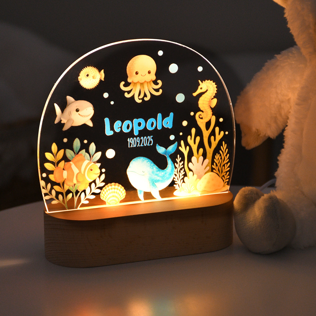 Beleuchtetes Nachtlicht mit Acrylplatte, Unterwassermotiv mit verschiedenen Meeresfiguren sowie dem personalisierten Namen „Leopold“ und dem Datum „19.09.2025“, aufgenommen in dunkler Umgebung.