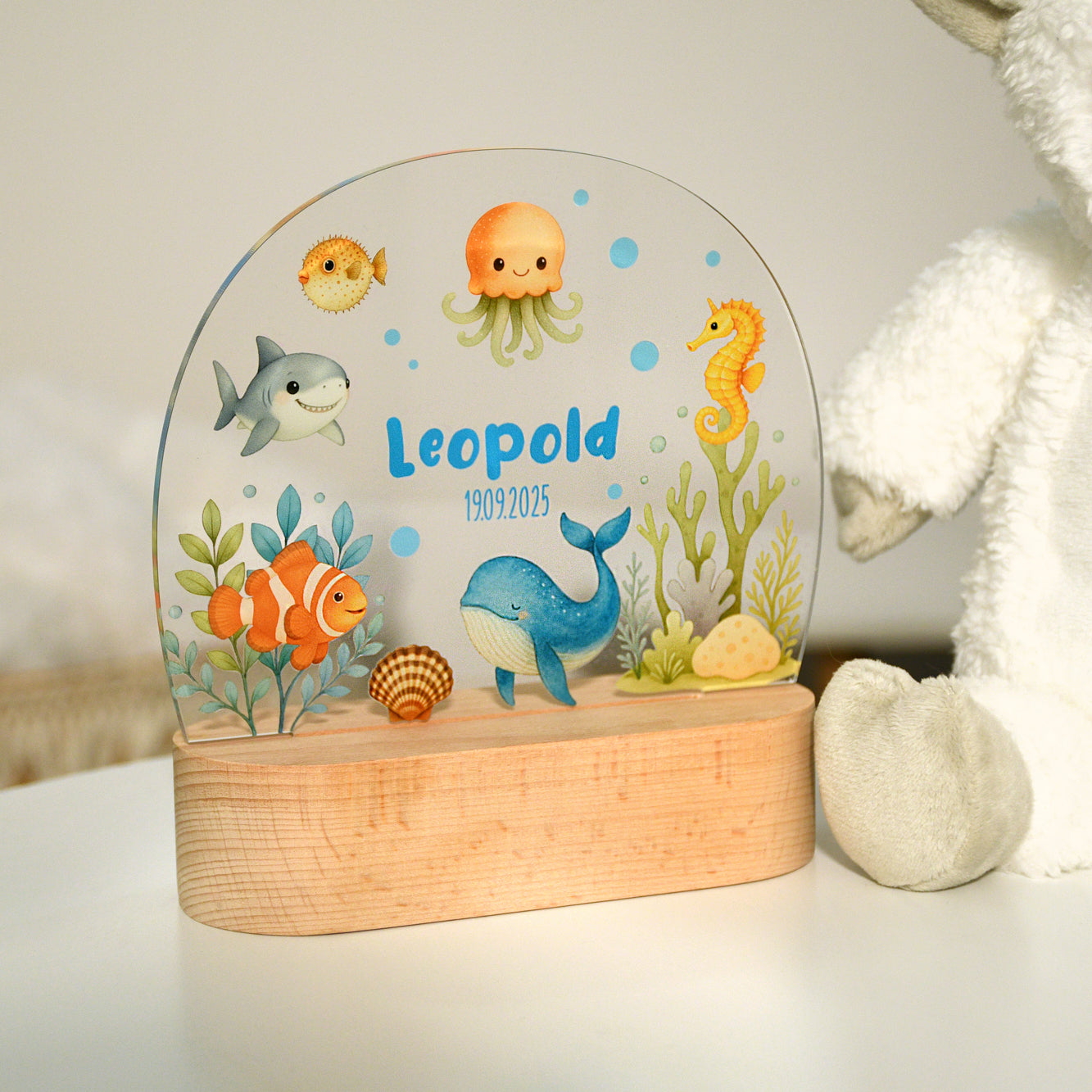 Unbeleuchtetes Nachtlicht mit Acrylplatte und Holzsockel aus Buche im Kinderzimmer, Unterwassermotiv mit Tieren wie Wal, Clownsfisch, Seepferdchen, Qualle und Kugelfisch, dargestellt in heller Umgebung.