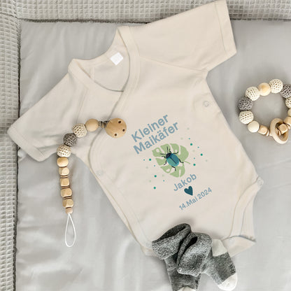 Baby Wickelbody natur, Kurzarm auf grauer Wickelunterlage, mit Kleiner Maikäfer in Bild und blauer Schrift, mit "Jakob" und "14. Mai. 2024" bedruckt