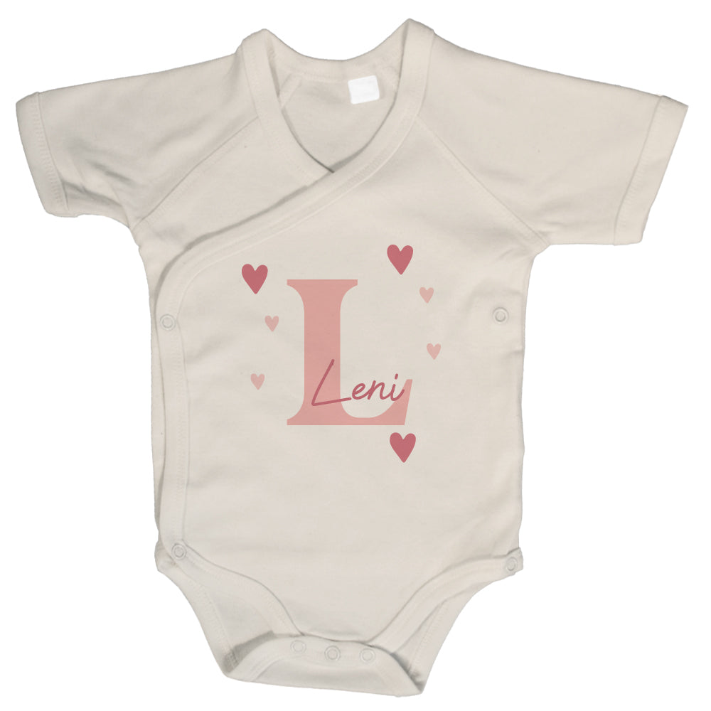Naturfarbener Wickelbody mit kurzem Arm, rosa Initiale „L“, Name „Leni“ und Herzmotiven auf weißem Hintergrund.