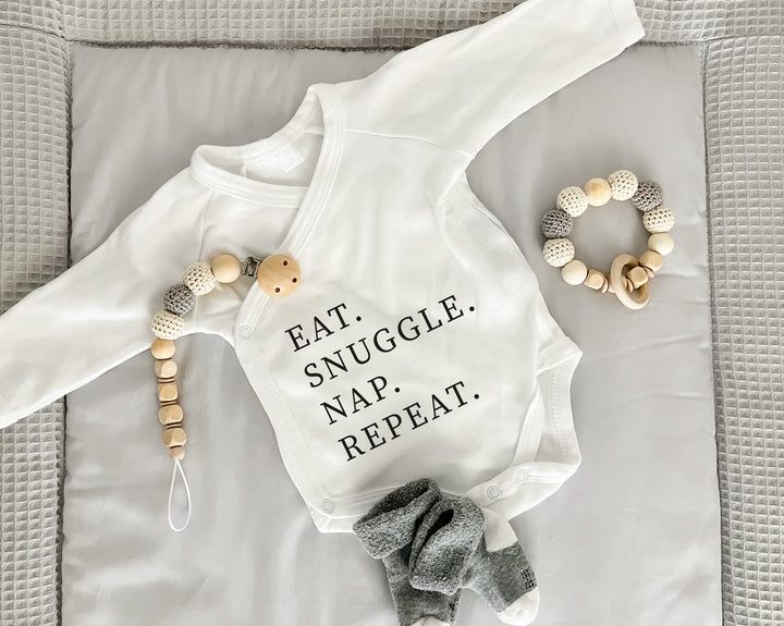 Premium Wickelbody | Spruch | Eat. Snuggle. Nap. Repeat | Langarm Body | Bio-Baumwolle | Geschenk zur Geburt mit Humor