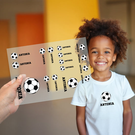 Kind trägt weißes T-Shirt mit aufgebügeltem Fußball-Motiv, darunter der personalisierte Name „Antonia“, Bügelbild-Bogen wird im Vordergrund gezeigt