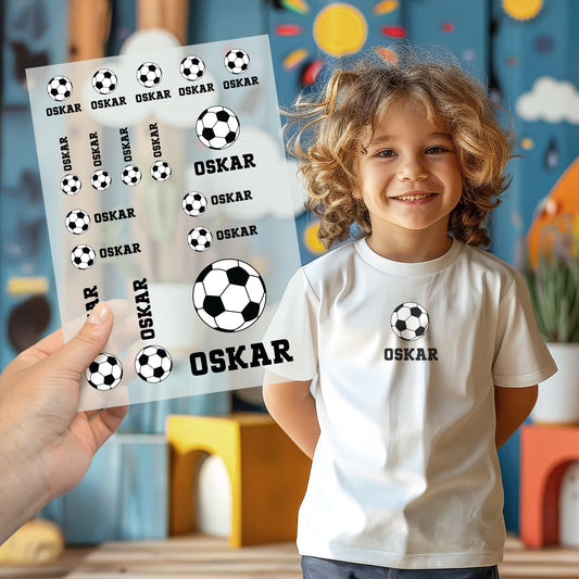 Kind trägt weißes T-Shirt mit aufgebügeltem Fußball-Motiv, darunter der personalisierte Name „Oskar“, Bügelbild-Bogen wird im Vordergrund gezeigt