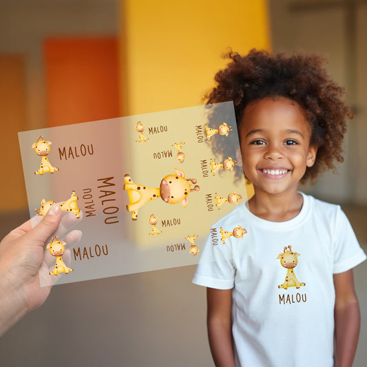 Kind trägt weißes T-Shirt mit aufgebügeltem Giraffen-Motiv und personalisiertem Namen „„Malou“, Bügelbild-Bogen wird im Vordergrund gezeigt