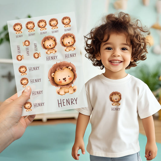 Kind trägt weißes T-Shirt mit aufgebügeltem Löwen-Motiv und personalisiertem Namen „Henry“, Bügelbild-Bogen wird im Vordergrund gezeigt