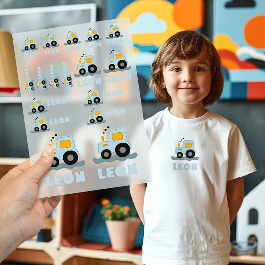 Kind trägt weißes T-Shirt mit aufgebügeltem Traktor-Motiv in blau, darunter der personalisierte Name „Leon“, Bügelbild-Bogen wird im Vordergrund gezeigt
