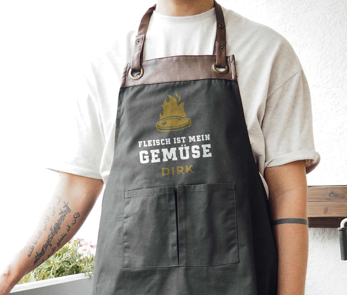 Person trägt schwarze Grillschürze mit braunem Lederbesatz, Aufdruck Fleisch ist mein Gemüse.