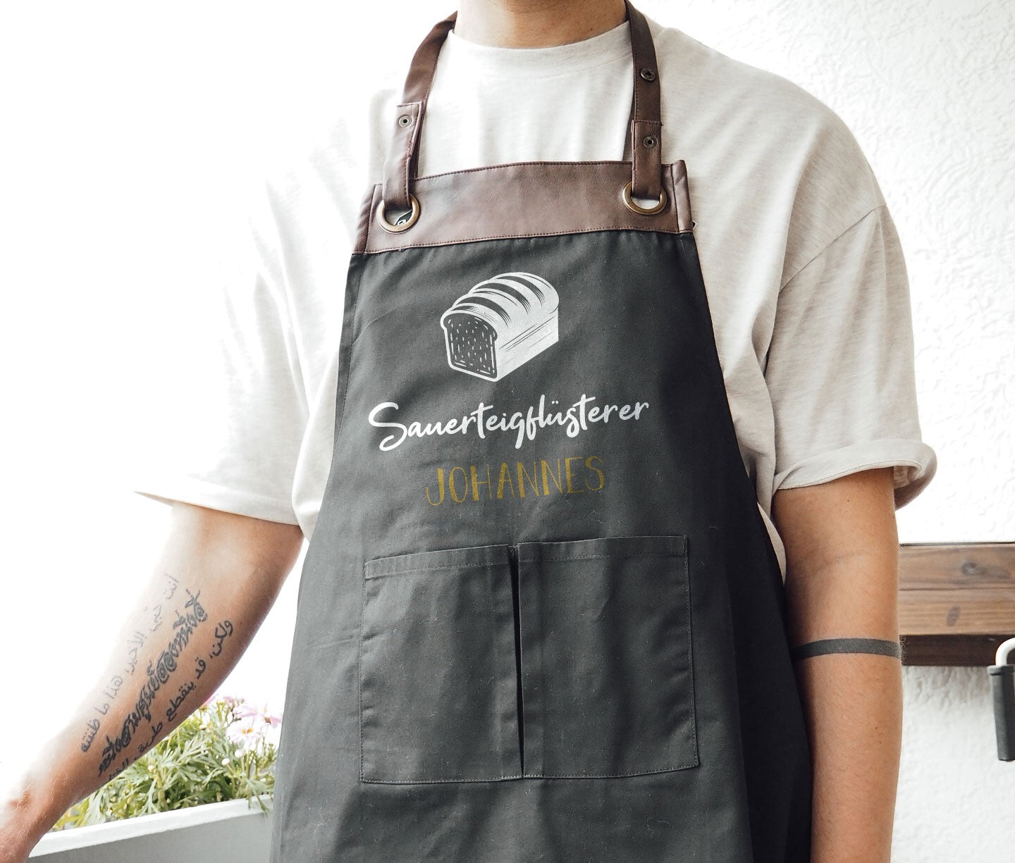 Personalisierte Backschürze mit Kunstleder Applikation „Sauerteigflüsterer“ in Beige oder Schwarz - verschenkich.de