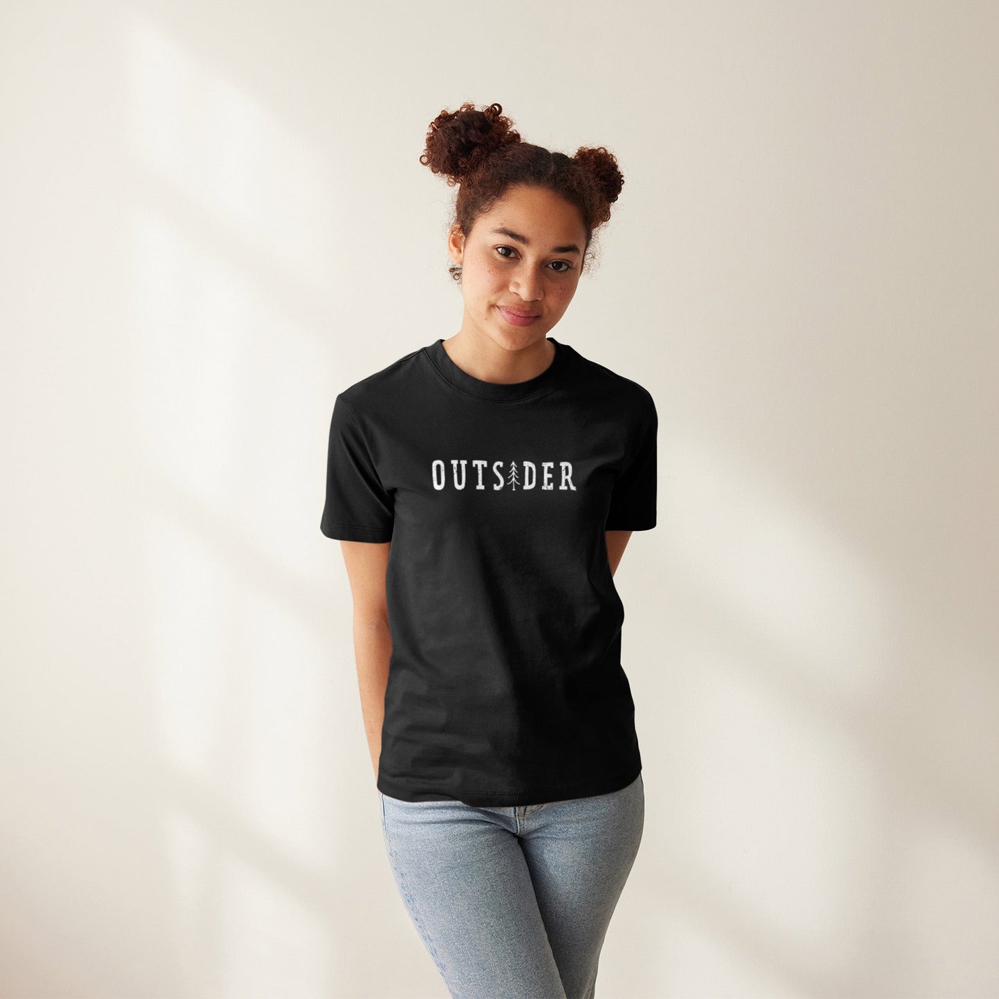 Modell trägt schwarzes T-Shirt mit Frontdruck „OUTSIDER“, bei dem das „i“ durch eine stilisierte Tanne ersetzt ist